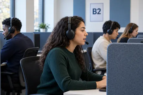 B2 işaretli bir dil sınavı salonunda kulaklıkla çalışan yetişkin adaylar